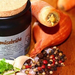 Gewürzregal mit bunten Gewürzen, Karotten und frischen Kräutern.